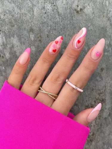 Este encantador diseño de uñas combina varios estilos para un look divertido y ecléctico. Algunas uñas presentan una suave base rosa, mientras que otras destacan con una base transparente adornada con múltiples corazones en tonos rosados o delicados patrones en espiral. La naturaleza caprichosa del diseño se realza con la colocación estratégica de un solo diamante rosado en el meñique, añadiendo un toque de glamour. Perfecto para quienes disfrutan expresando su personalidad alegre a través de su estilo, este diseño es ideal tanto para las festividades de San Valentín como para un toque de moda en el día a día.