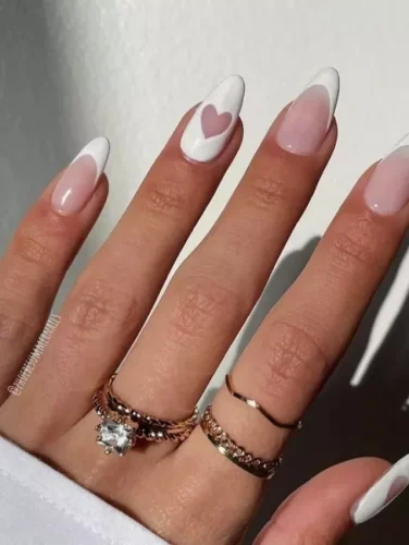 Este sofisticado diseño de uñas le da un toque romántico a la clásica manicura francesa, con puntas blancas definidas sobre una base rosa translúcida para un look atemporal. Una uña de acento destaca con un corazón en negativo, fusionando sutilmente el minimalismo moderno con un encanto elegante. Perfecto para quienes aman una estética chic y refinada, este diseño es ideal para ocasiones especiales, compromisos o una celebración de San Valentín con estilo.