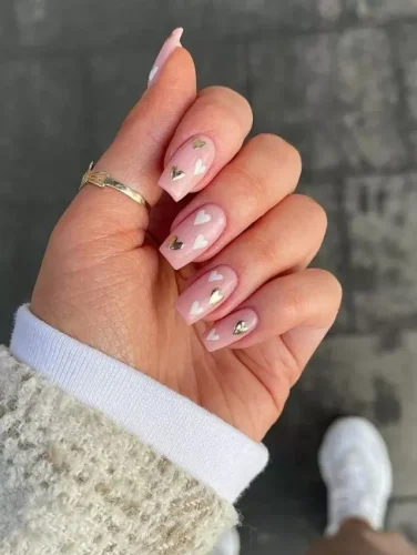 Este elegante diseño de uñas presenta una suave base rosa rubor adornada con delicados corazones blancos y dorados metálicos, creando una estética soñadora y femenina. El acabado brillante realza los sutiles pero sofisticados detalles, mientras que la forma cuadrada de las uñas añade un toque de modernidad. Perfecto para quienes aman el lujo discreto, este diseño es ideal para el Día de San Valentín, eventos nupciales o cualquier ocasión donde el romance se encuentre con el estilo refinado.