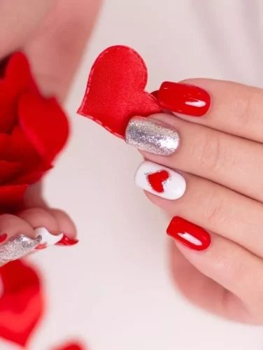 Este deslumbrante diseño de uñas para San Valentín combina el romance clásico con un toque moderno. El audaz esmalte rojo brillante aporta un estilo apasionado, mientras que las uñas de acento plateadas brillantes ofrecen un contraste chic. Una uña blanca con un detalle de corazón recortado realza el tema lleno de amor, haciendo que esta manicura sea perfecta para una noche romántica o una celebración festiva. Con su estética juguetona pero elegante, ¡este diseño seguramente cautivará corazones!