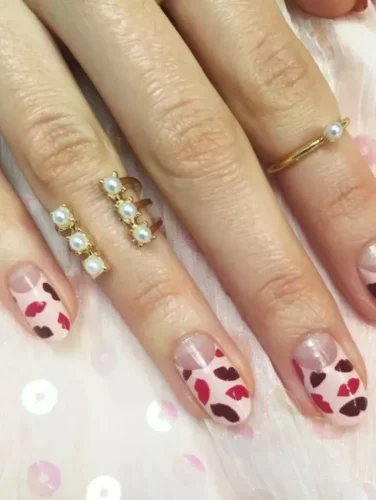 Estas uñas elegantes pero juguetonas presentan una base nude con delicadas impresiones de labios rojos y burdeos, creando una vibra romántica y coqueta. El diseño de espacio negativo añade un toque moderno, lo que lo convierte en una opción perfecta para una manicura de San Valentín sutil pero estilosa. Combinado con anillos dorados acentuados con perlas, este look es tanto sofisticado como trendy.