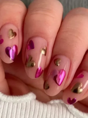 Este chic diseño de Uñas de San Valentín 2025 presenta una base nude brillante adornada con vibrantes corazones metálicos en tonos de rosa y dorado. Los acentos reflectantes crean un impresionante efecto 3D, añadiendo un toque de glamour a un look suave y romántico. Perfecto para quienes aman una mezcla de elegancia y audacia en su arte de uñas.