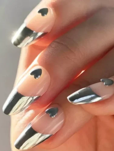 "Elegancia plateada" ofrece una interpretación sofisticada y contemporánea del diseño de uñas para San Valentín, combinando el encanto clásico con estéticas modernas. Este estilo presenta una base nude que transiciona sin problemas hacia puntas metálicas plateadas impactantes, creando un aspecto chic y pulido.

La adición de pequeños corazones negros en la base de cada uña proporciona un guiño sutil al tema de San Valentín, haciendo que este diseño sea ideal para aquellos que prefieren un arte de uñas minimalista pero elegante. Es perfecto tanto para eventos formales como para salidas casuales en torno al Día de San Valentín.