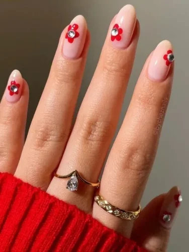 Este elegante diseño de uñas para San Valentín presenta delicados acentos florales rojos sobre una suave base nude. Cada pequeña flor está adornada con una brillante piedra de estrás en su centro, añadiendo un toque de glamour y sofisticación. El look minimalista pero llamativo es perfecto para quienes aman una manicura sutil pero festiva para la temporada del amor. ¡Ideal para una celebración chic y romántica de San Valentín!