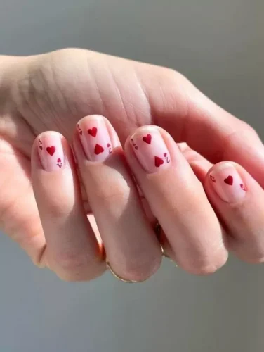 Este delicado y juguetón diseño de uñas para San Valentín presenta pequeños corazones rojos y garabatos caprichosos sobre una base nude translúcida. El look minimalista pero encantador da la ilusión de notas de amor escritas a mano, haciéndolo perfecto para una vibra romántica y divertida de San Valentín. ¡Este diseño es ideal para quienes aman el arte de uñas sutil y artístico, con un toque de amor en cada detalle!