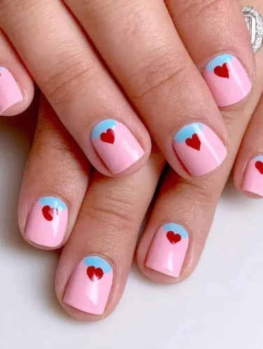 Este adorable diseño de Uñas de San Valentín 2025 presenta una suave base rosa con una delicada punta francesa azul bebé, creando un efecto de cielo soñador. Cada uña está adornada con un pequeño corazón rojo, añadiendo un toque de romance y diversión. ¡Perfecto para quienes aman un look dulce, minimalista y chic con un giro único en el clásico tema de San Valentín!