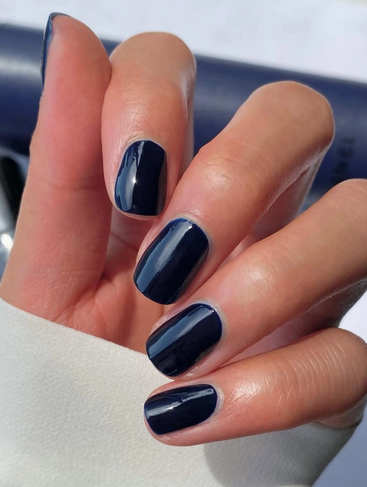 Uñas azul oscuro brillantes con esmalte Chanel Le Vernis, representando los colores de uñas de invierno en tendencia.