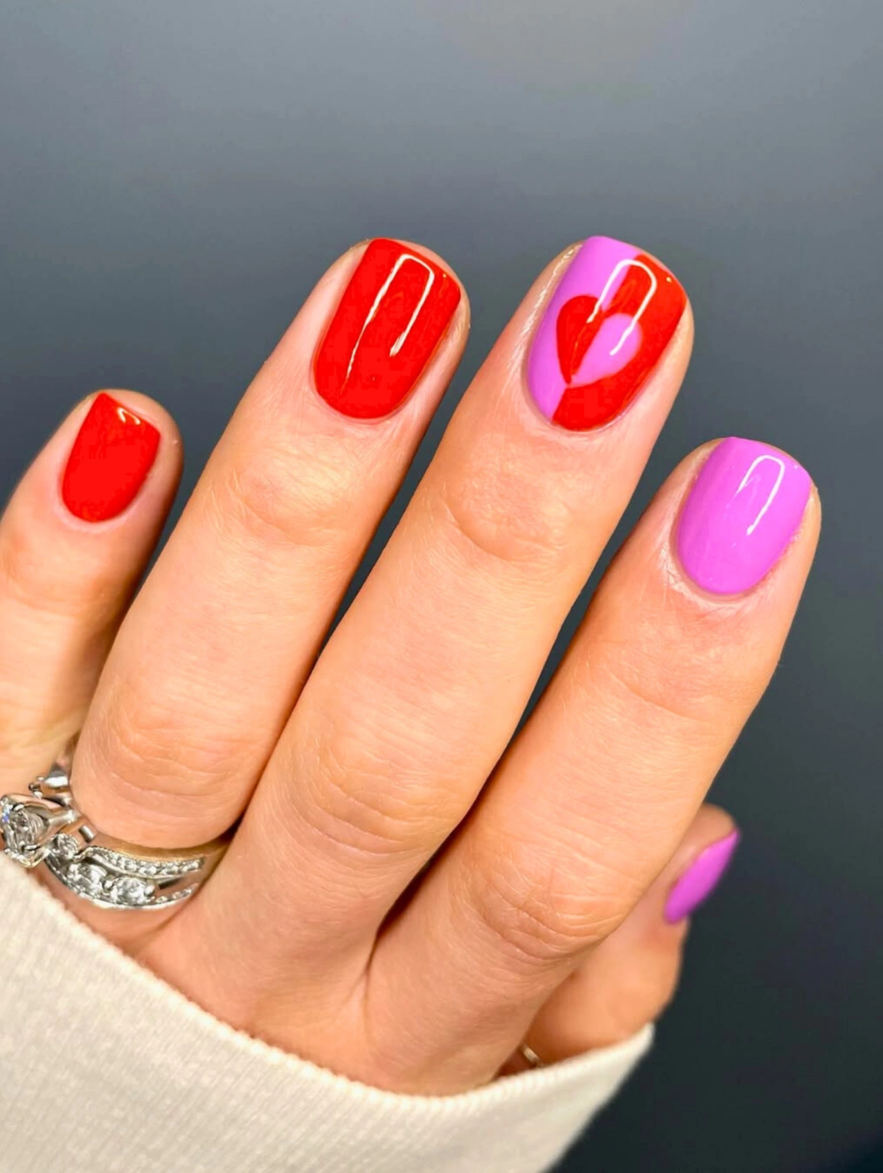 Easy DIY Valentine’s Day Nail Art featuring bold red and pink polish with a heart accent on short rounded nails