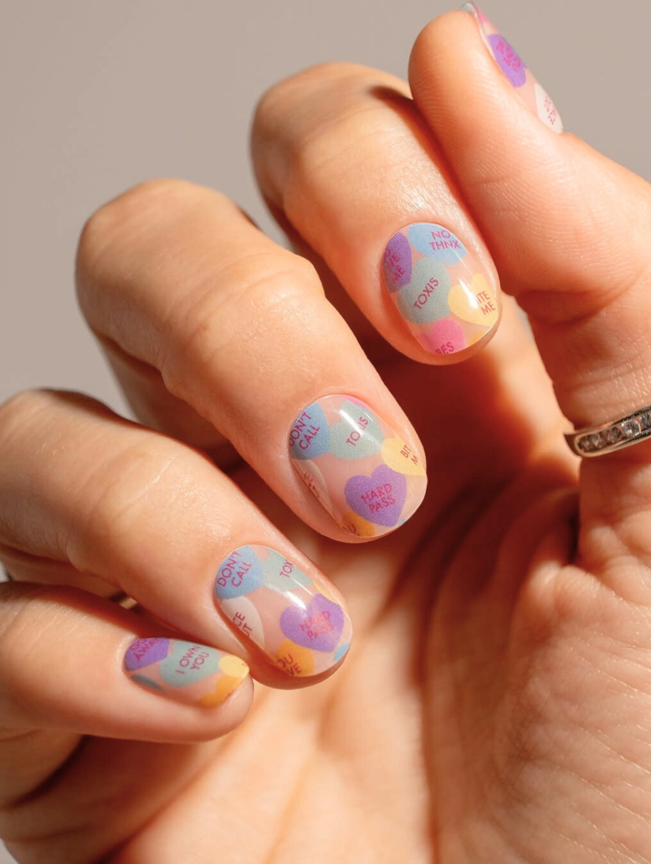 Easy DIY Valentine’s Day Nail Art featuring pastel conversation heart designs with candy-inspired phrases on short, natural nails