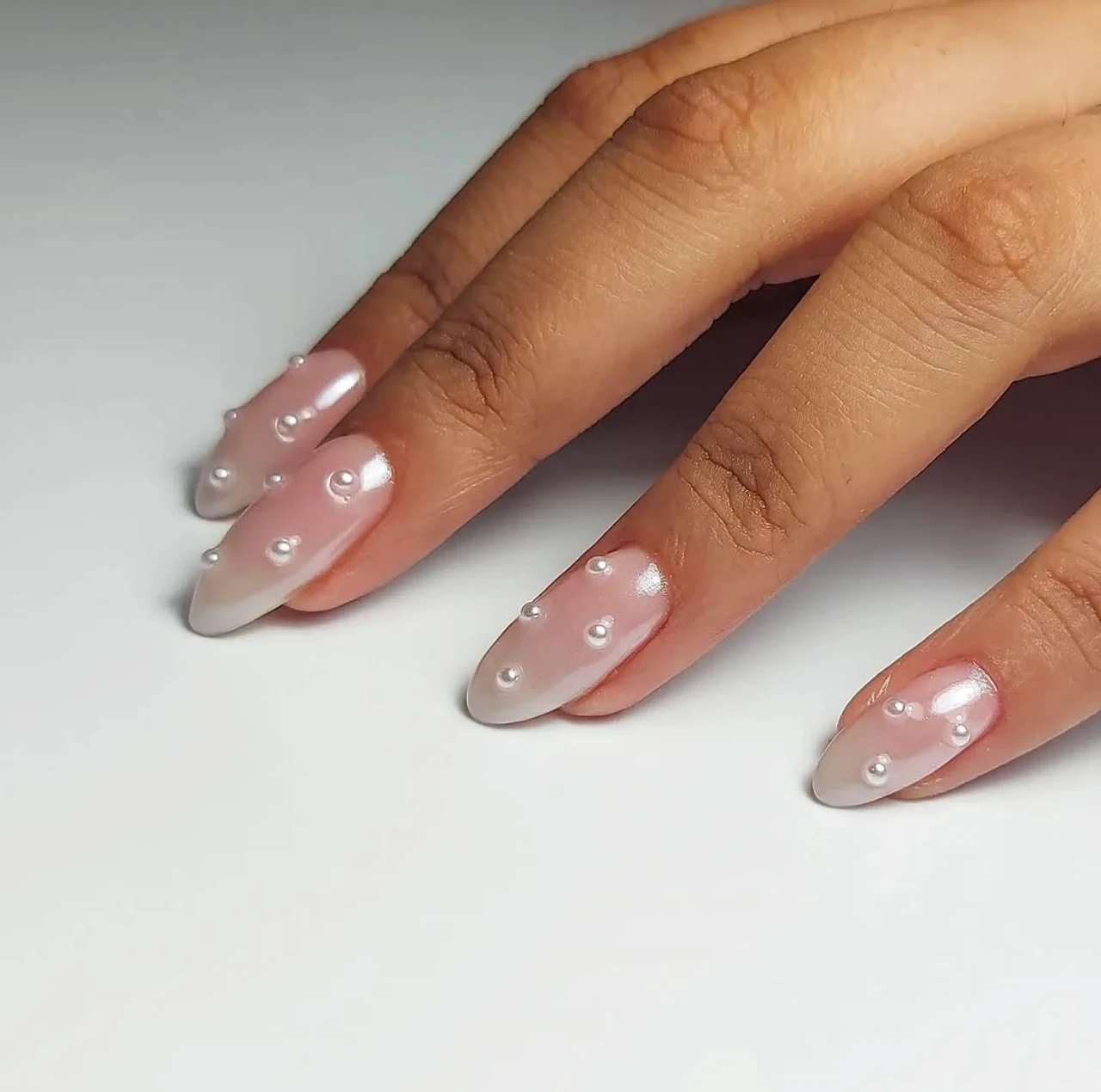 Diseño de uñas elegancia perlada minimalista con perlas pequeñas sobre base rosada nacarada.