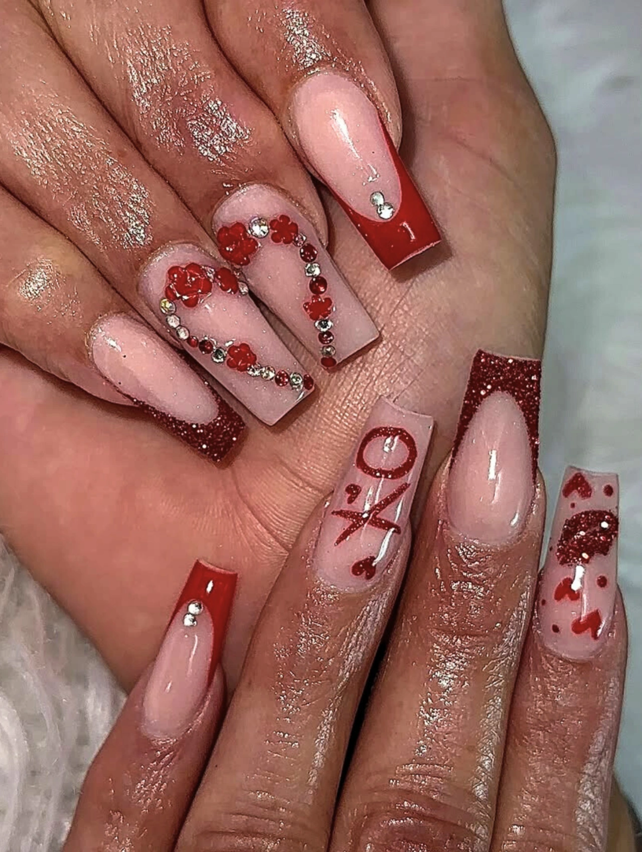 Red XO Rhinestone Coffin Valentine’s Nails with glossy nude bases, red accents, and sparkling rhinestone details.