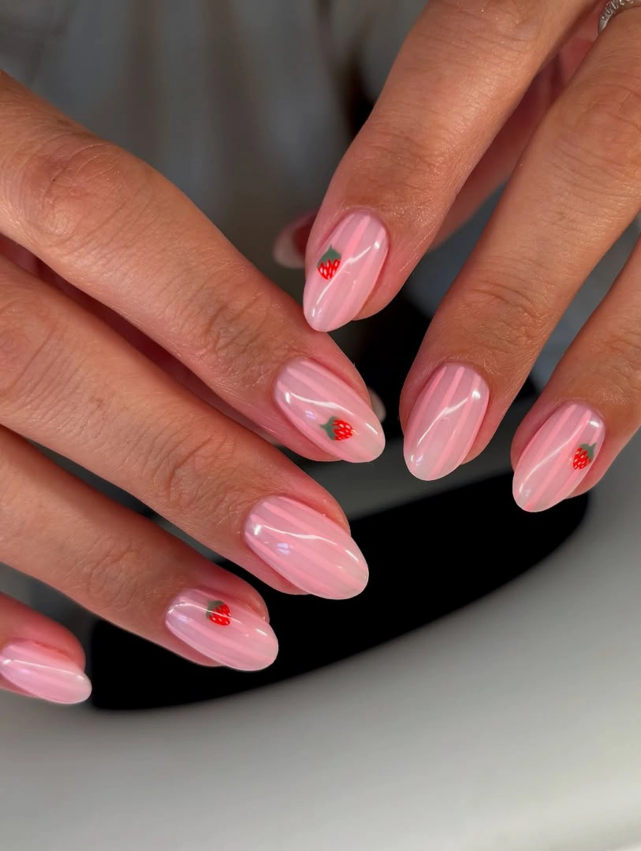 Soft Pink Strawberry Valentineโs Nails Almond with almond-shaped pink nails and tiny strawberry nail art accents.