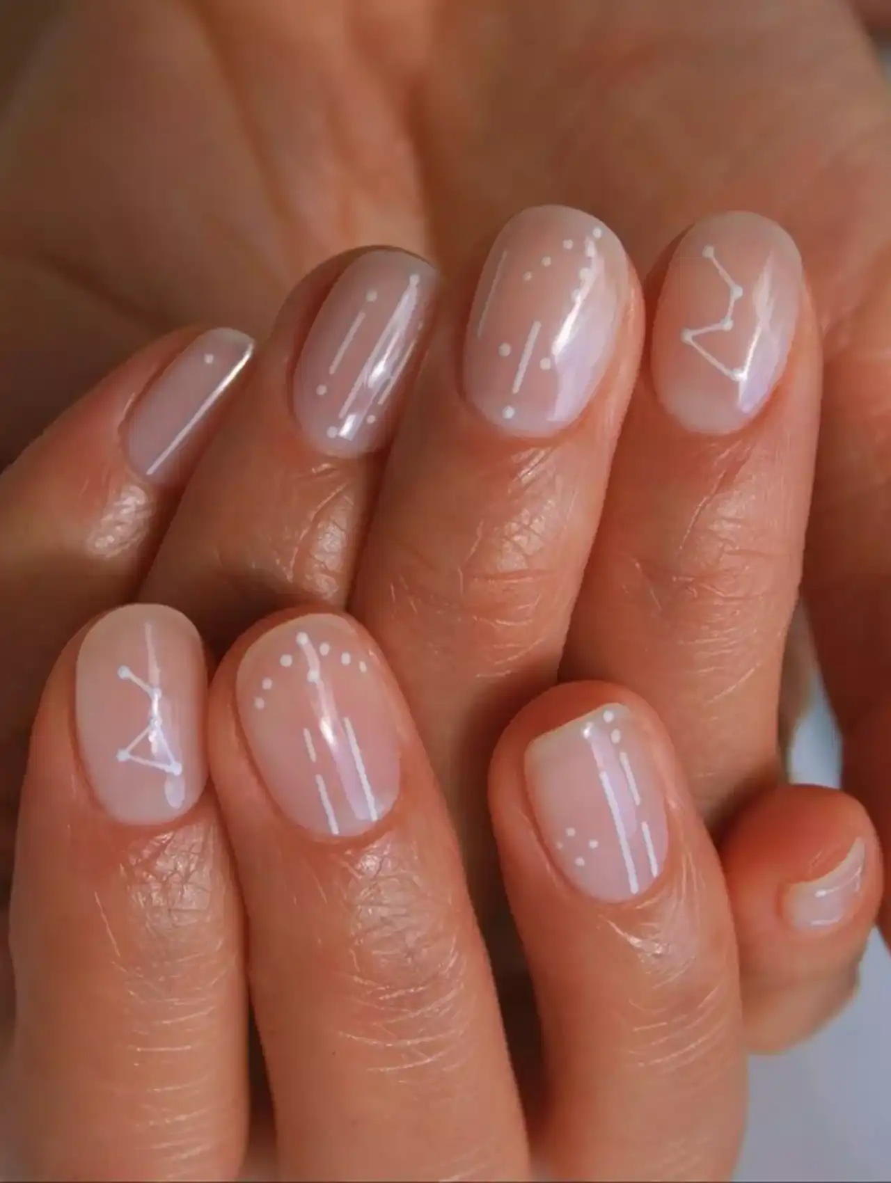 Short nude nails with white nail polish constellation and star designs.