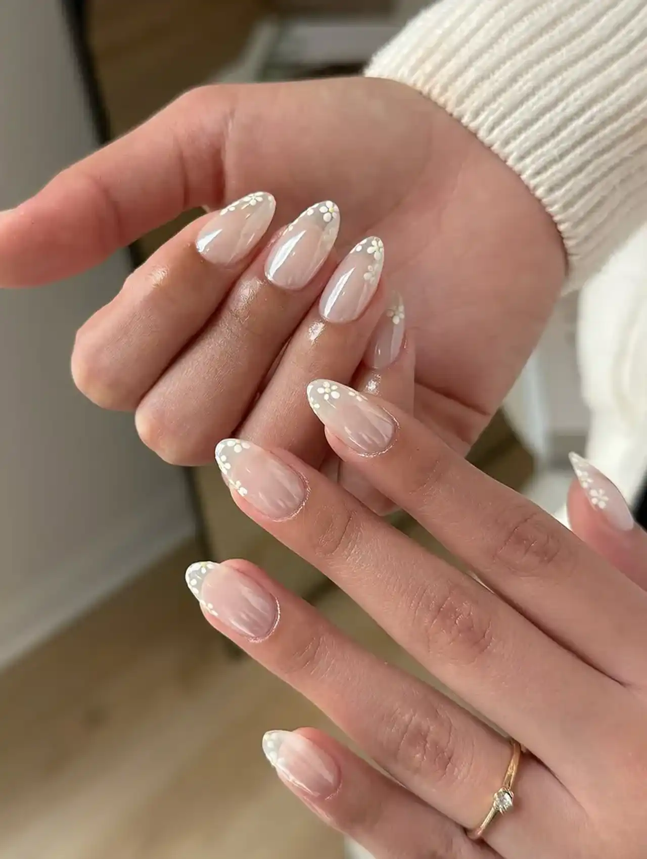 Sheer almond nails with white nail polish French tips and small daisy accents.