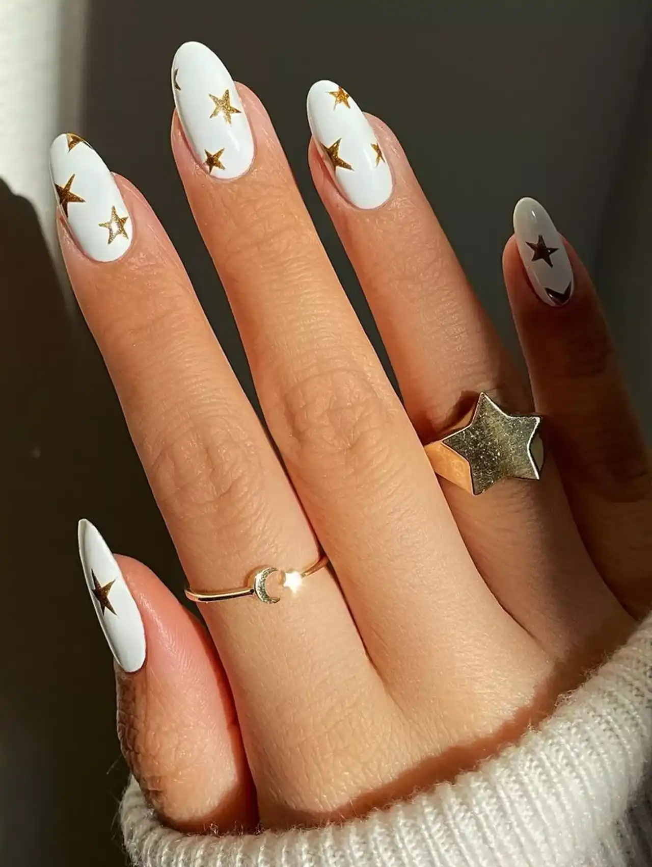 White nail polish with gold star accents on oval-shaped nails, creating a chic celestial manicure.