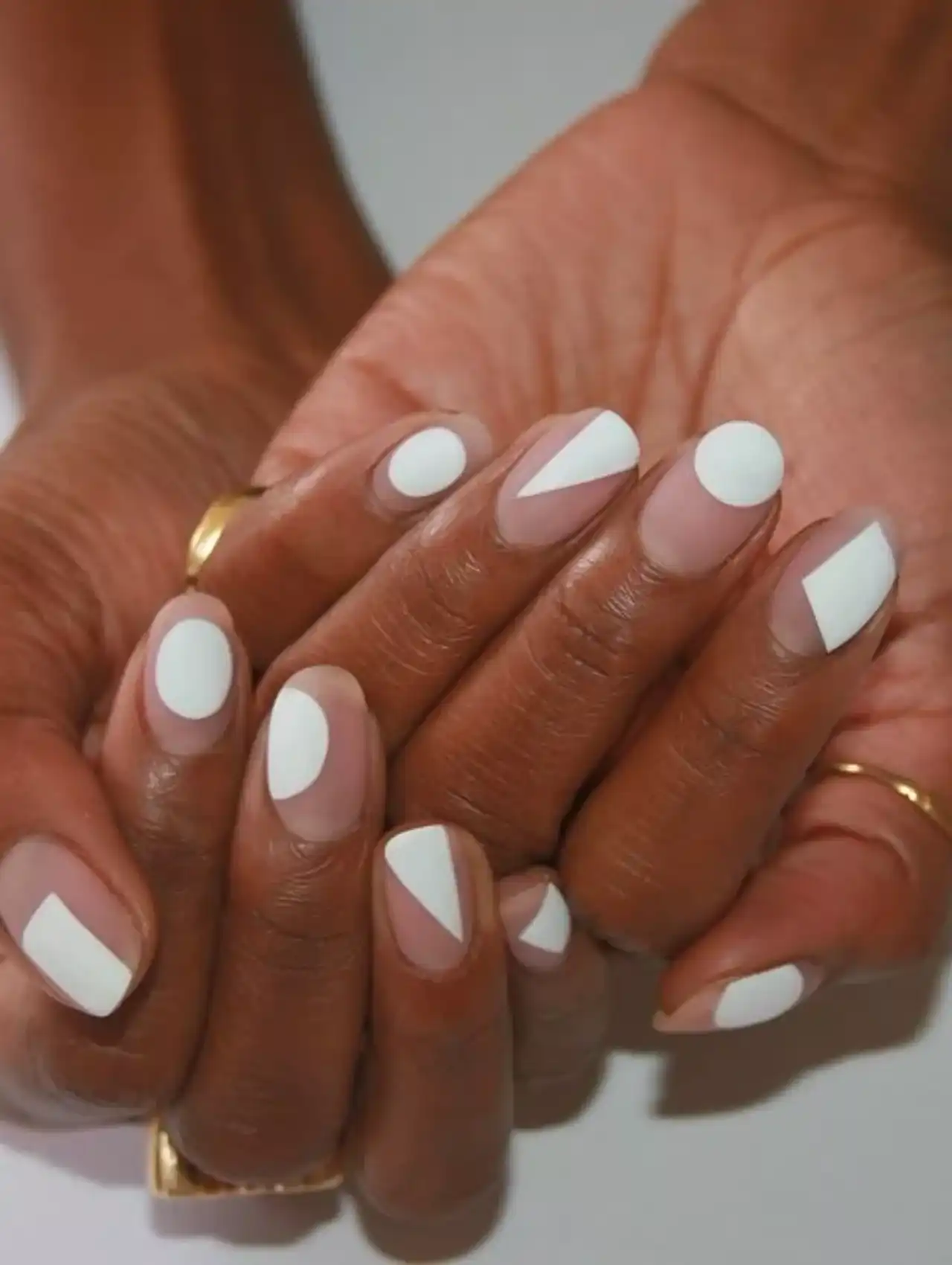 Matte white nail polish with abstract negative space shapes on natural nails.