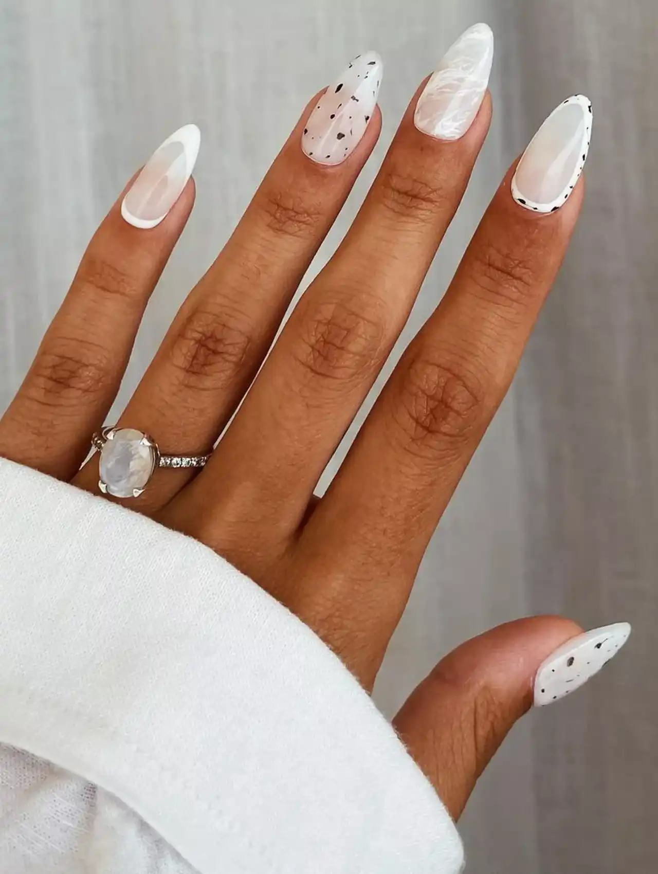 Milky white nail polish with marbled designs and black spot accents.