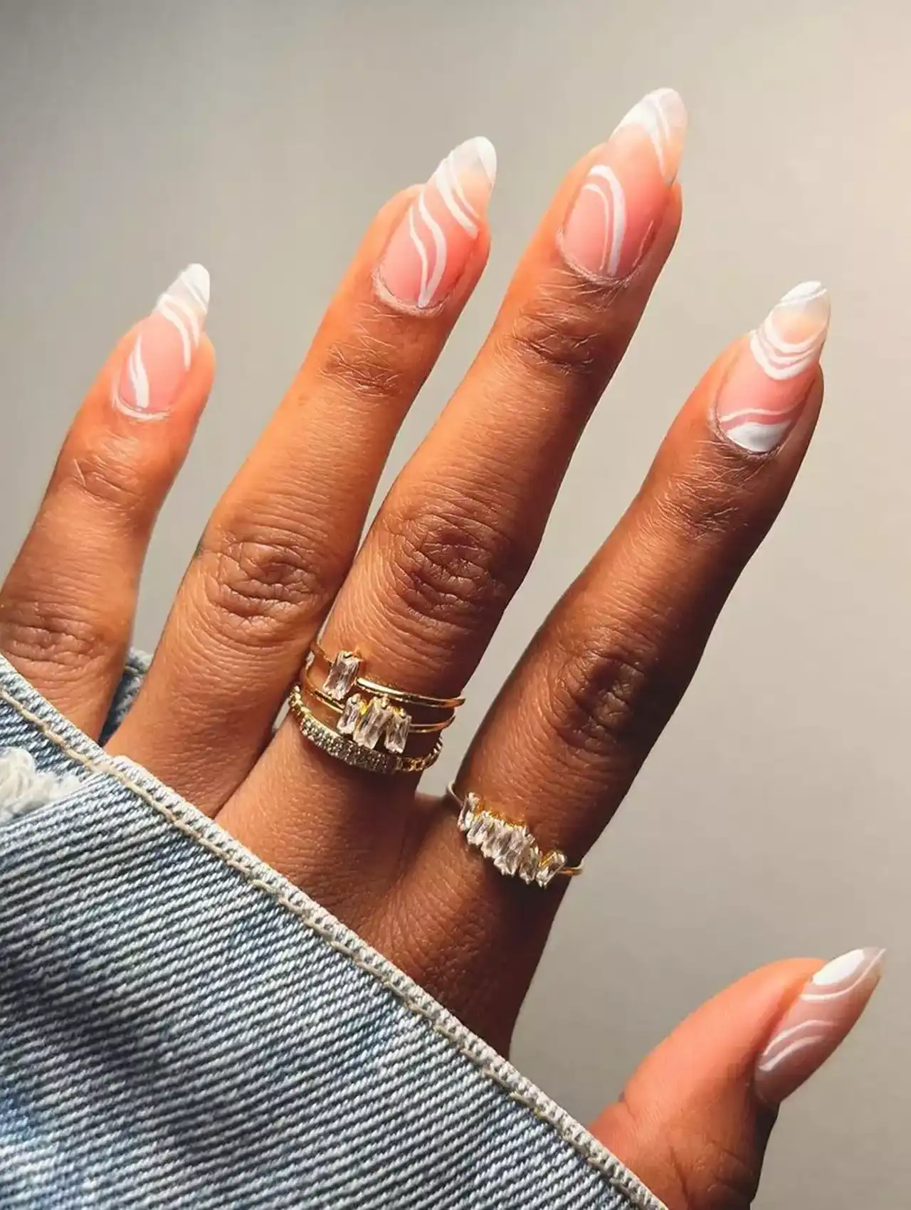 Nude nails with white nail polish swirl patterns and almond shape.