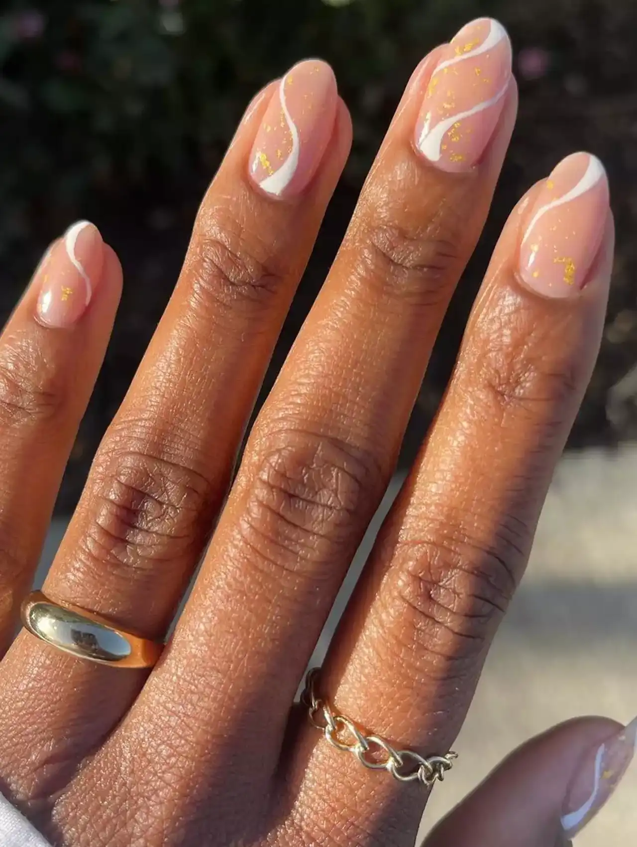 Nude nails with wavy white polish lines and gold flakes.