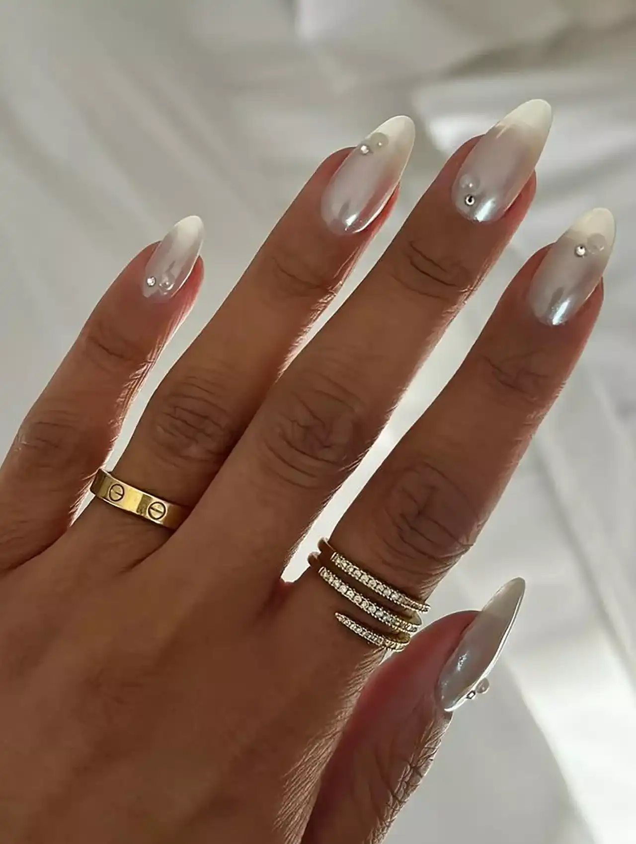 White ombré nail polish with small silver studs on almond nails.