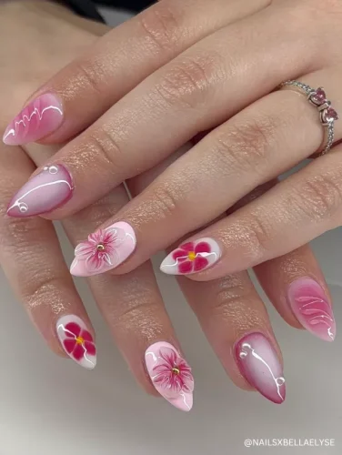 Elegant pink stiletto nails featuring 3D floral designs, white swirl accents, and a glossy ombré finish.