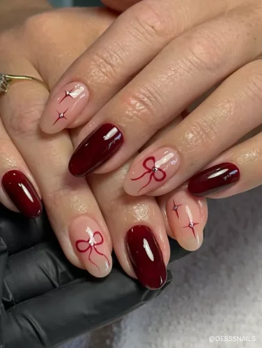 A chic holiday-inspired manicure featuring glossy deep red and nude nails with delicate red bow and star accents.