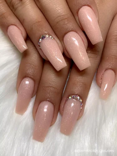 Elegant coffin-shaped nude nails with a soft shimmer and delicate rhinestone accents for a touch of understated glamour.