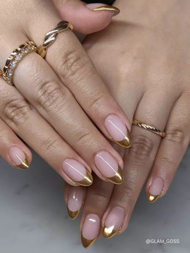 Nude almond nails with metallic gold French tips.
