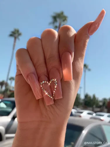 Glossy nude coffin nails featuring a delicate rhinestone heart design on the ring finger for a romantic and elegant touch.