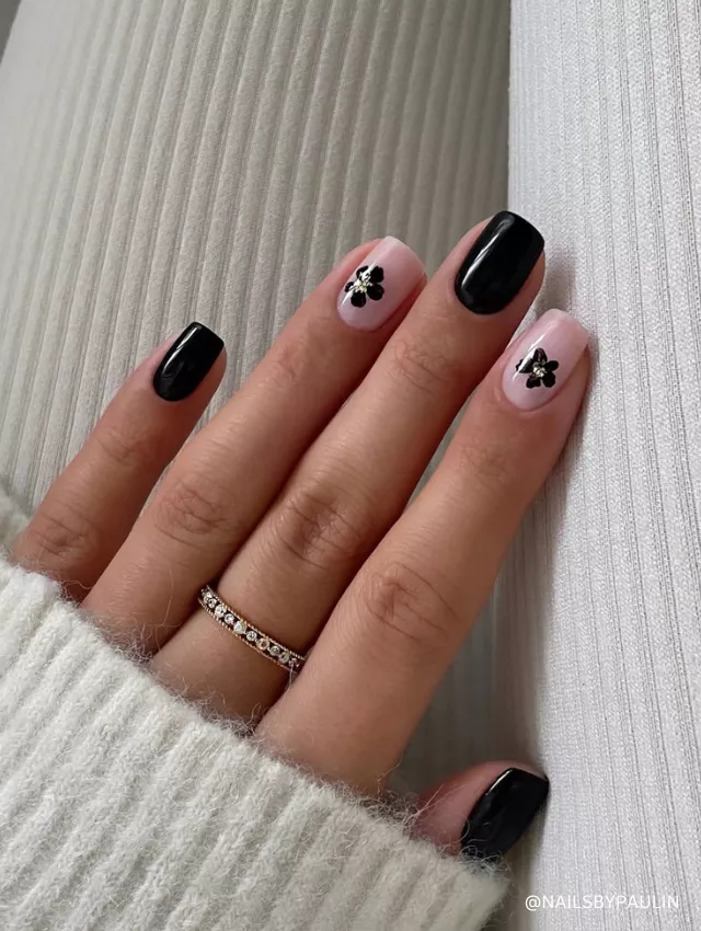 A chic black and nude nail design featuring glossy black polish and delicate floral accents.