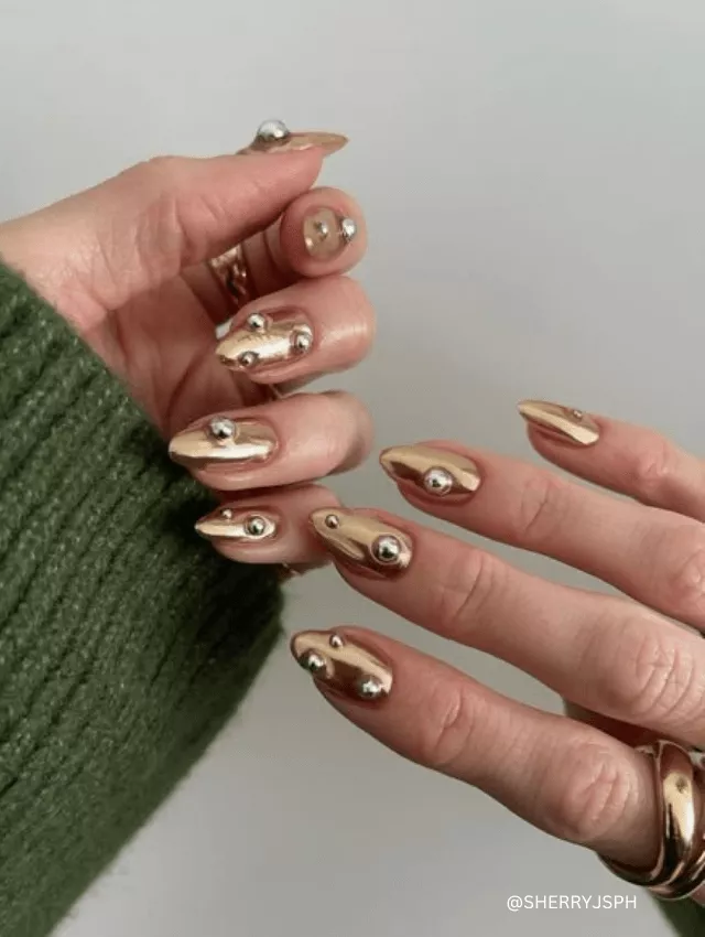 Almond-shaped gold chrome nails with 3D silver bead accents.