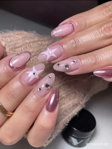 Chic pink and nude almond nails featuring 3D stars, rhinestone embellishments, and a glossy metallic accent.