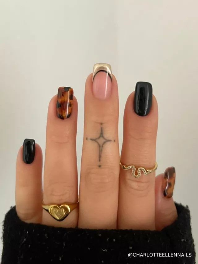 A stylish nail design featuring black, tortoiseshell patterns, and a gold-accented French tip.