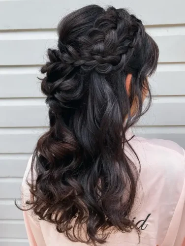 This hairstyle exudes romance with its half-up, half-down design featuring a braided crown that transitions into flowing, cascading curls. The rich, dark hair is enhanced by subtle highlights that catch the light, adding depth and a luxurious sheen. This style is perfect for special occasions, blending classic braiding with loose curls to create a look that’s both enchanting and sophisticated. Ideal for those who want to combine the elegance of braids with the softness and femininity of free-flowing curls. 🌸✨