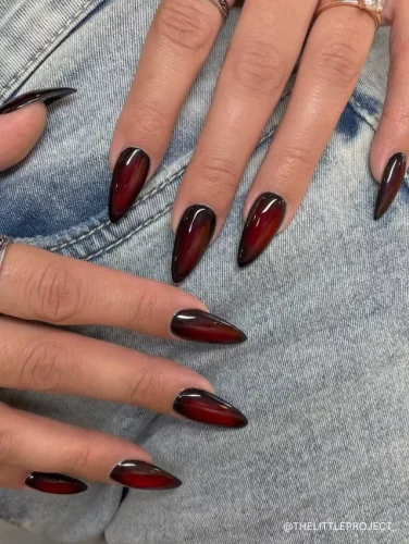 A bold and edgy stiletto manicure featuring a black-to-deep-red ombre design with a glossy finish.