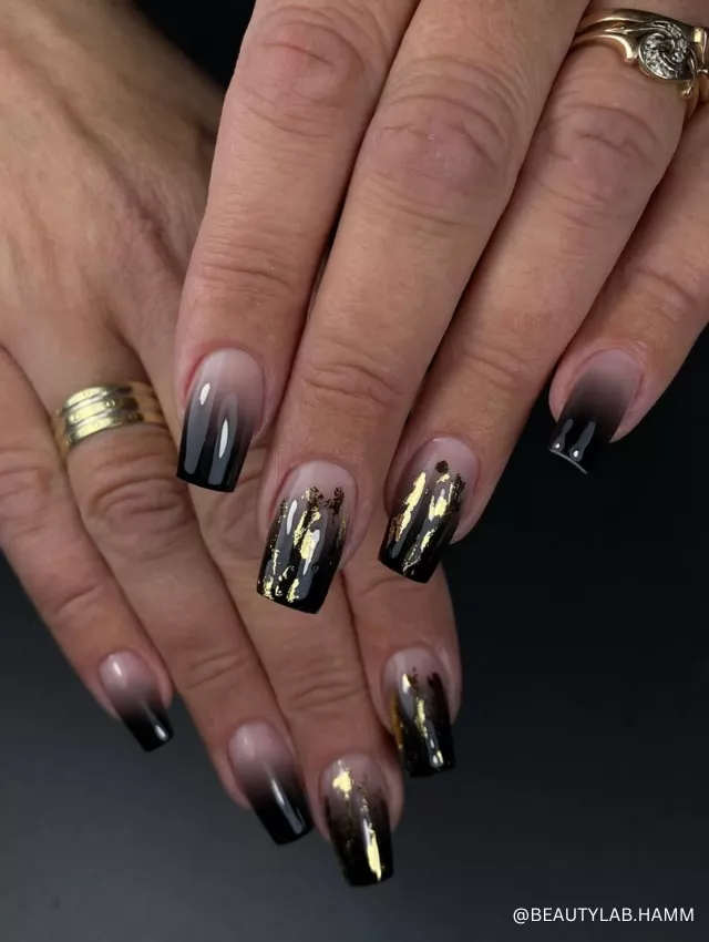 A luxurious black ombre nail design with gold foil accents and a glossy finish.