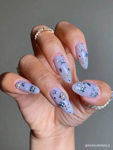 Elegant almond-shaped nails with an icy blue base, adorned with pearls, blue rhinestones, and delicate silver embellishments for a frosty, winter-inspired look.