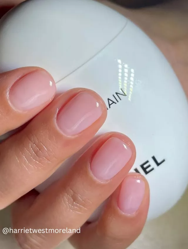 Close-up image of a hand holding a designer beauty product, displaying chic soap nails with a soft pink gloss.