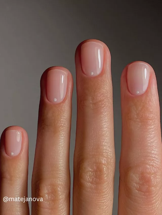 Close-up view of soap bubble nails, featuring a subtle pink polish with a single white dot on each nail.