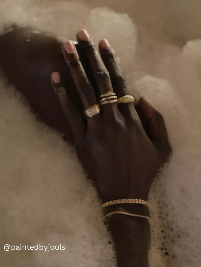 A hand adorned with jewelry, submerged in foam, showcasing a classic Soap Nails manicure.