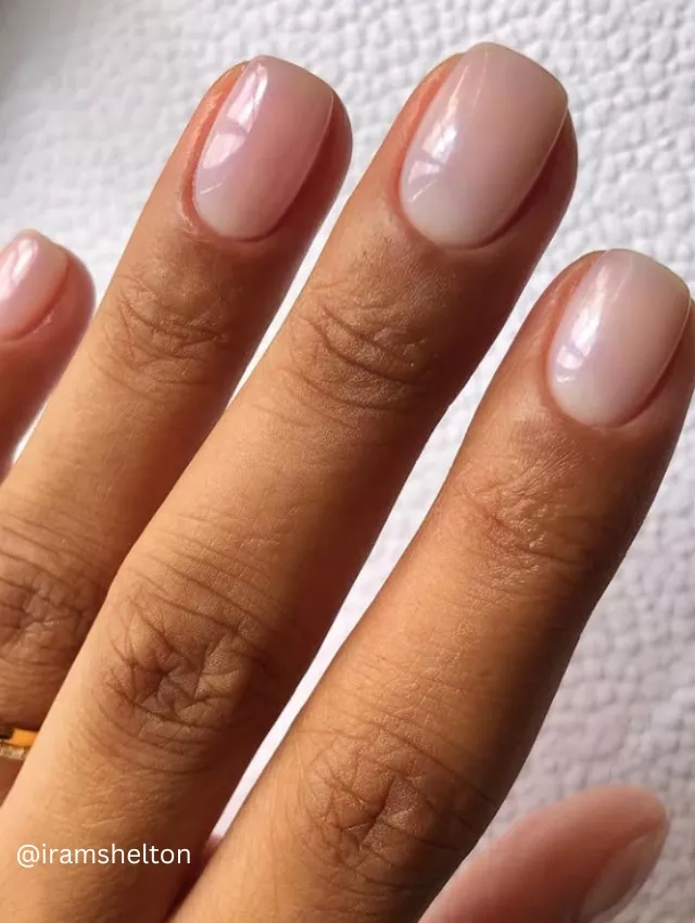 A hand adorned with jewelry, submerged in foam, showcasing a classic Soap Nails manicure.