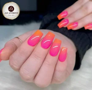 Close-up of neon pink and orange ombre acrylic nails with a glossy finish.