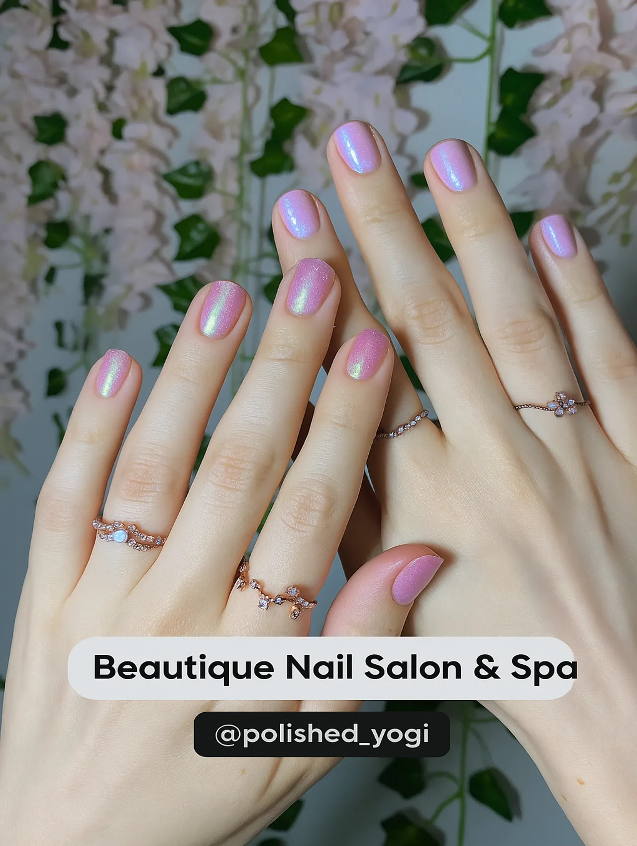 Close-up of both hands with iridescent pink pearl nails from Beautique Nail Salon & Spa, surrounded by soft floral decor.