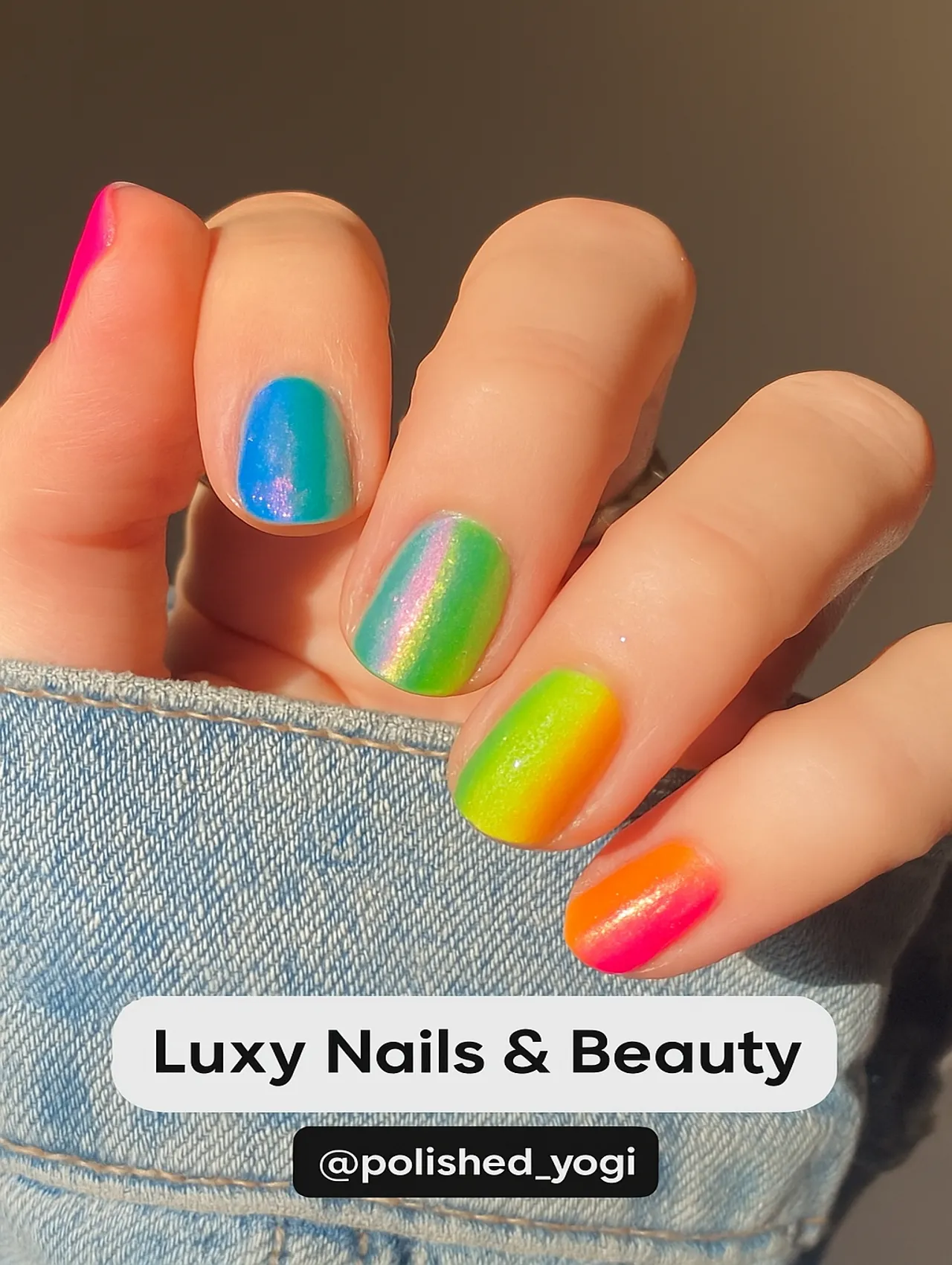 Close-up of a hand with short iridescent rainbow nails from Luxy Nails & Beauty, featuring a bright, shimmering gradient.