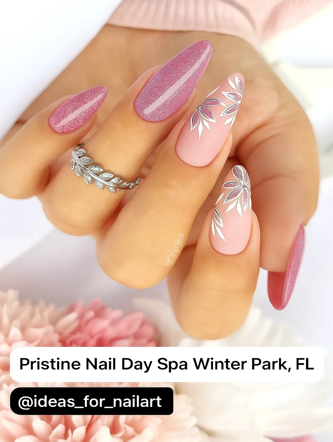 A close-up of pink glitter and floral nail art from Pristine Nail Day Spa in Winter Park, FL, featuring almond-shaped nails with silver accents.