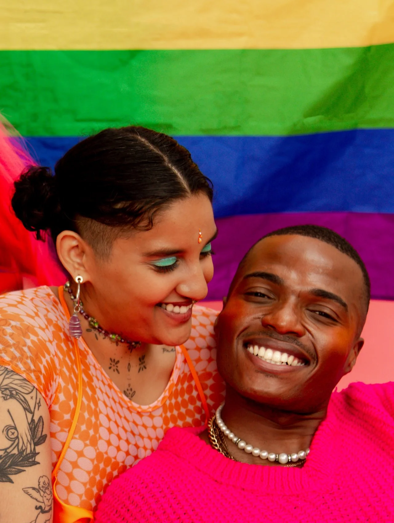 Two people smiling together in front of a rainbow Pride flag, representing gender inclusive services and LGBTQ+ welcoming spaces in Orlando