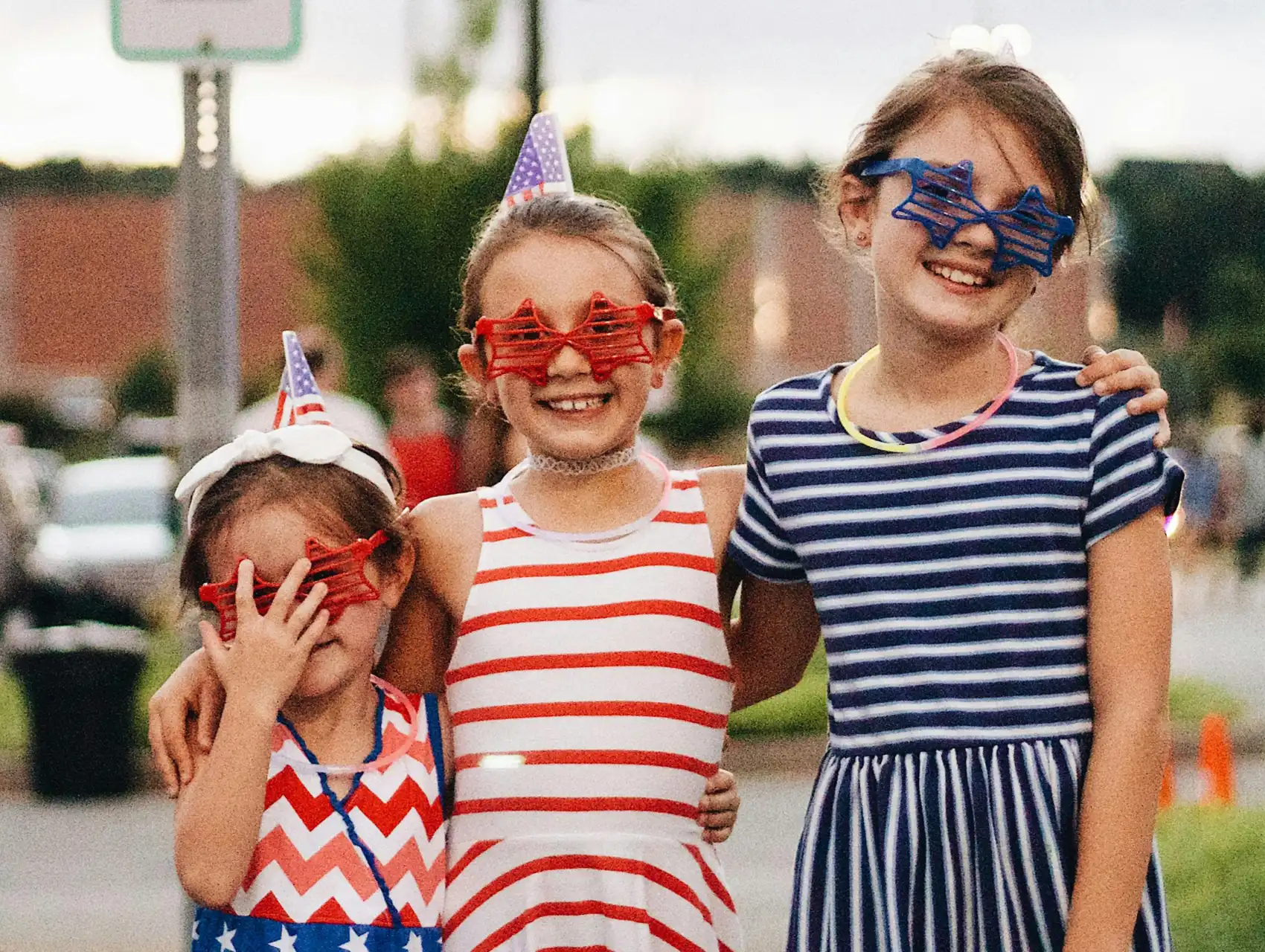 Three young girls in festive red, white, and blue outfits enjoying 4th of July in Orlando with star-shaped glasses.