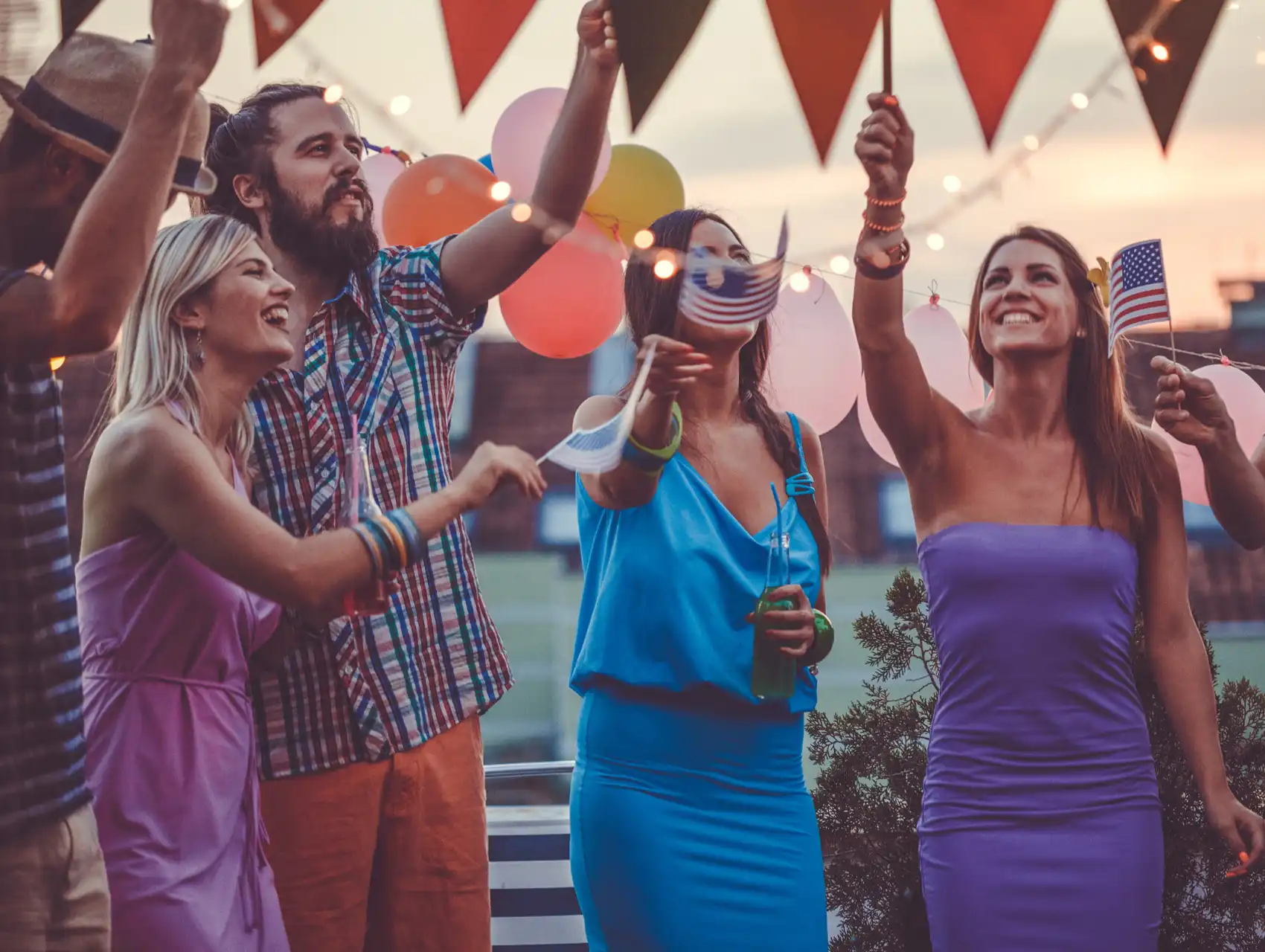 Group of young adults at a rooftop 4th of July Orlando party waving American flags and enjoying the celebration.