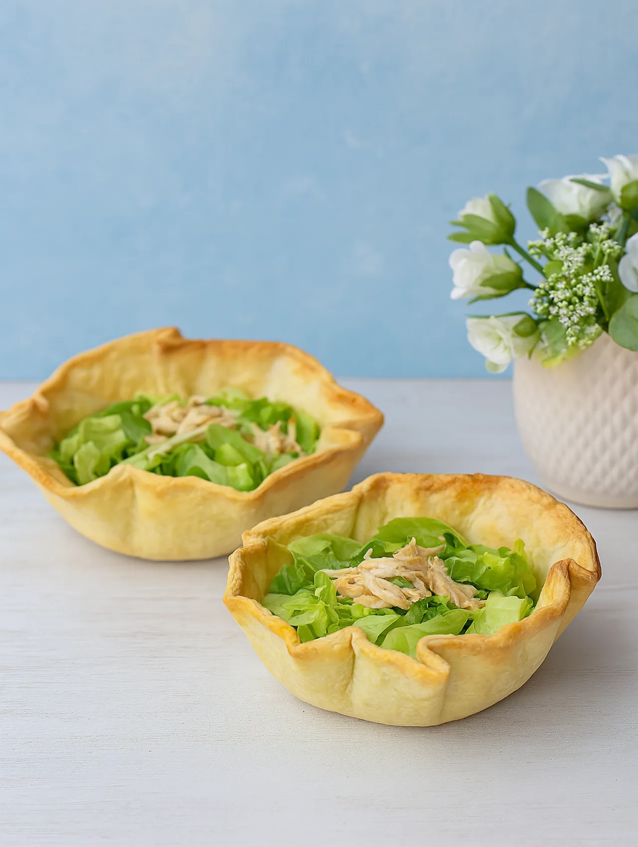 Canastitas de hojaldre rellenas de ensalada de pollo fría sobre mesa clara con decoración floral