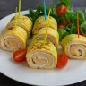 Rollitos de tortilla rellenos de jamón y queso, servidos con ensalada fresca y tomates cherry sobre un plato blanco.